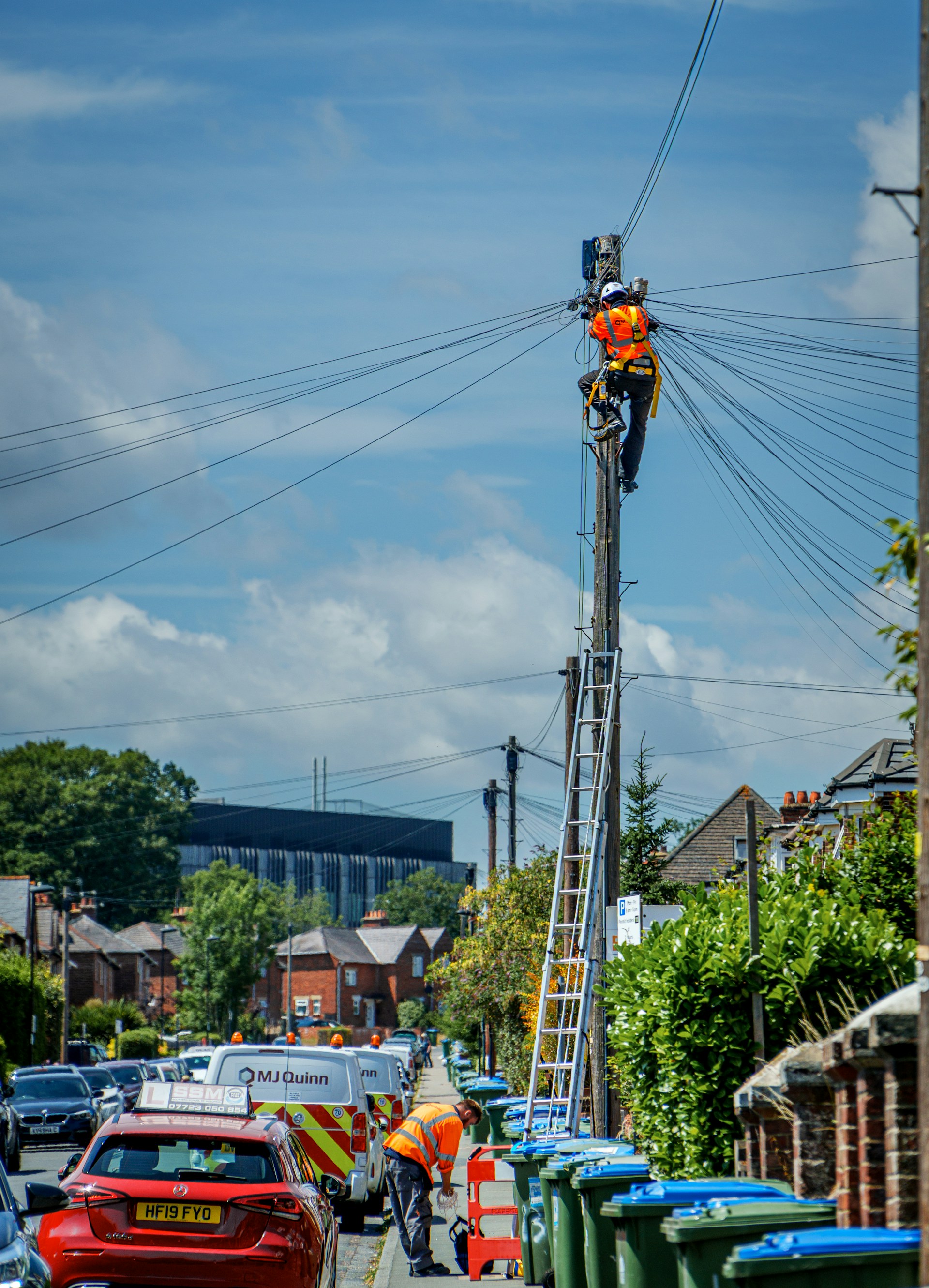 Lineman in a hard hat and harness working at the top of a utility pole