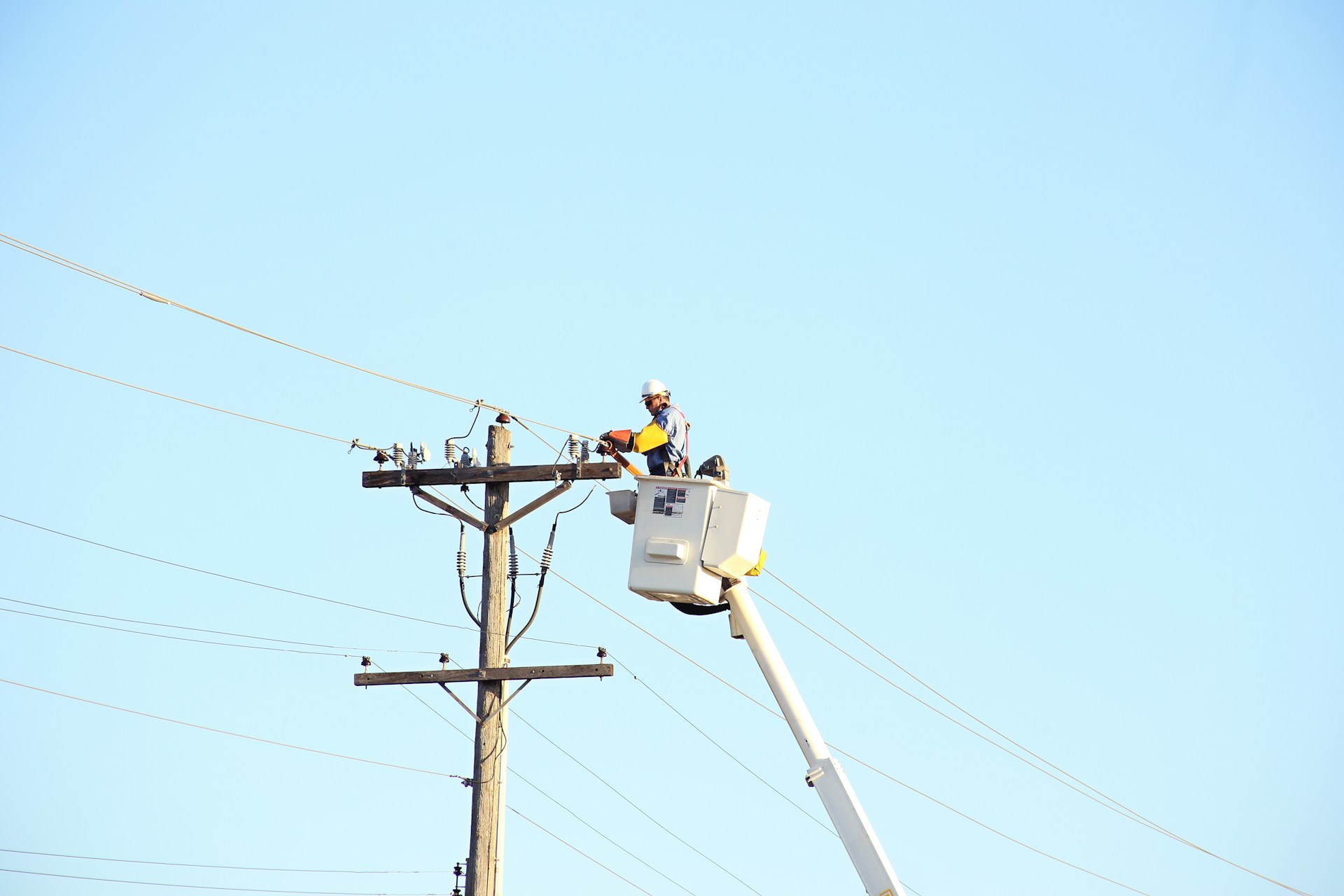 Utility lineman in a high-visibility jacket working on overhead lines above a neighborhood